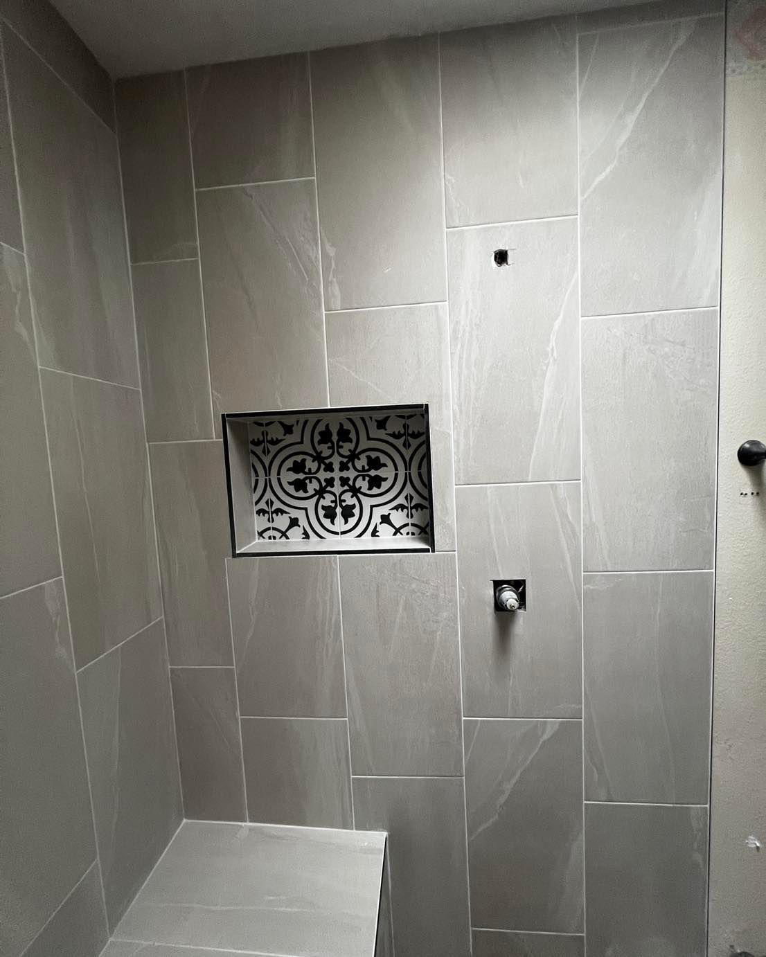 Gray tiled shower with decorative niche and fixtures.