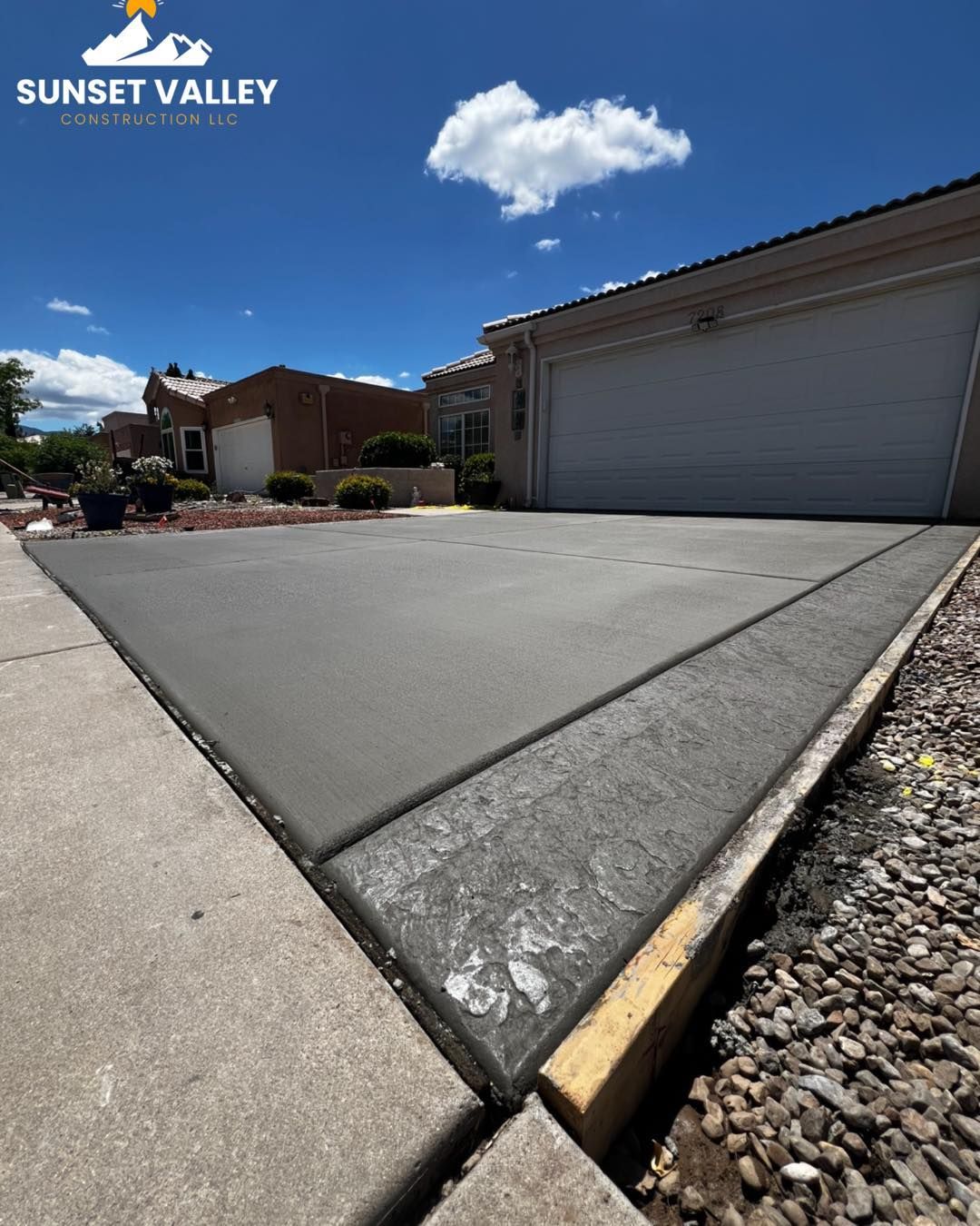 Newly poured concrete driveway next to a sidewalk and a house with a garage on a sunny day.