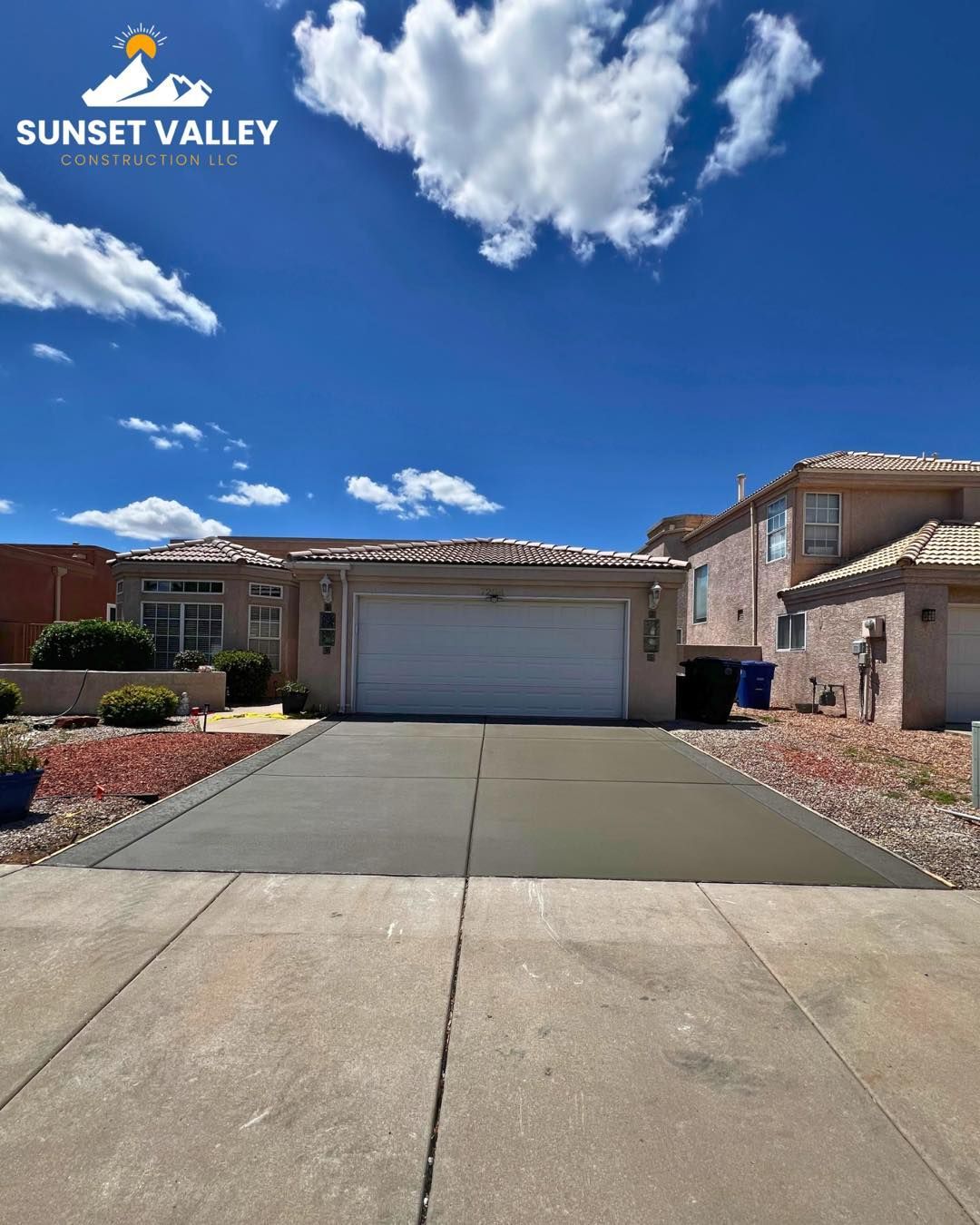 House with a newly poured concrete driveway under a blue sky with clouds.
