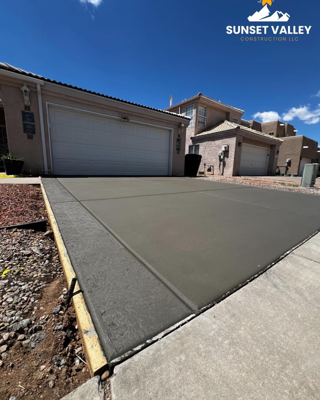 Freshly poured concrete driveway in front of a house, set in a residential neighborhood on a sunny day.