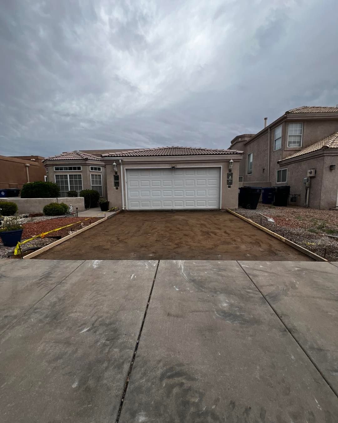 Driveway leading to a home with a garage.  The area in front of the garage is dirt. Overcast sky.