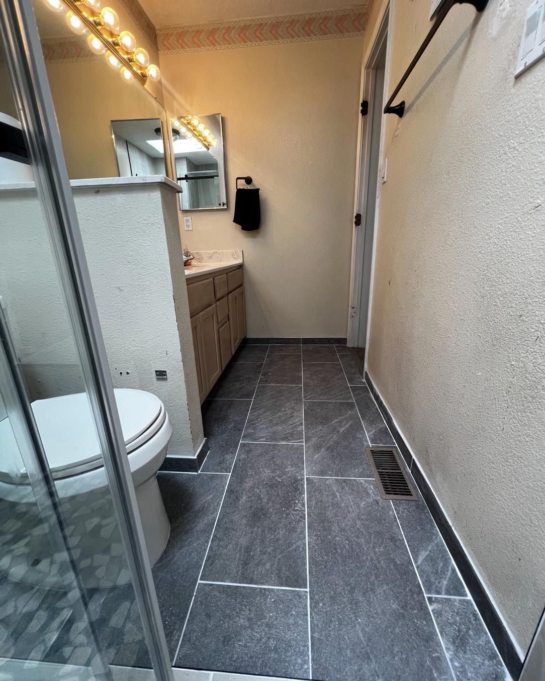 Bathroom with dark gray floor tiles, light-colored walls, and a vanity. A shower and toilet are visible.