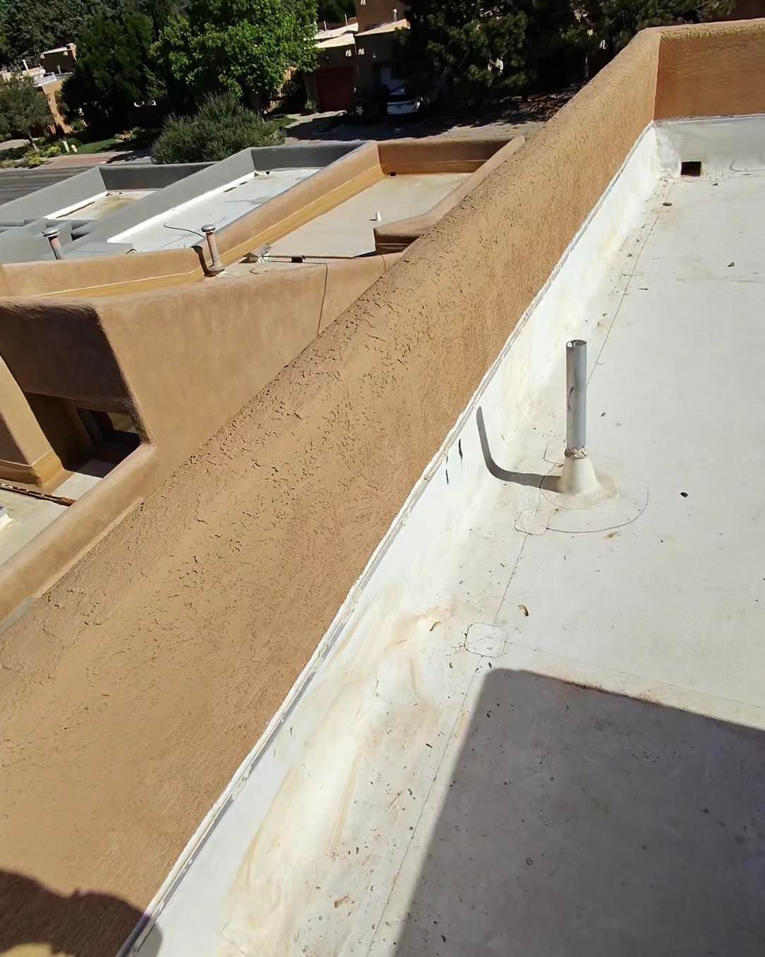 Adobe-style building rooftop with a raised edge, pale white roof, and ventilation pipe.