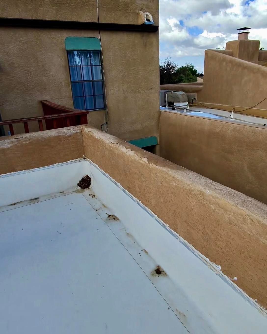 View from rooftop, looking toward tan stucco buildings with blue-framed window and a flat roof.