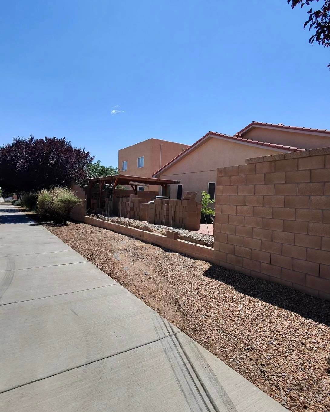 Residential buildings with tan walls, brown brick wall, sidewalk, and blue sky.