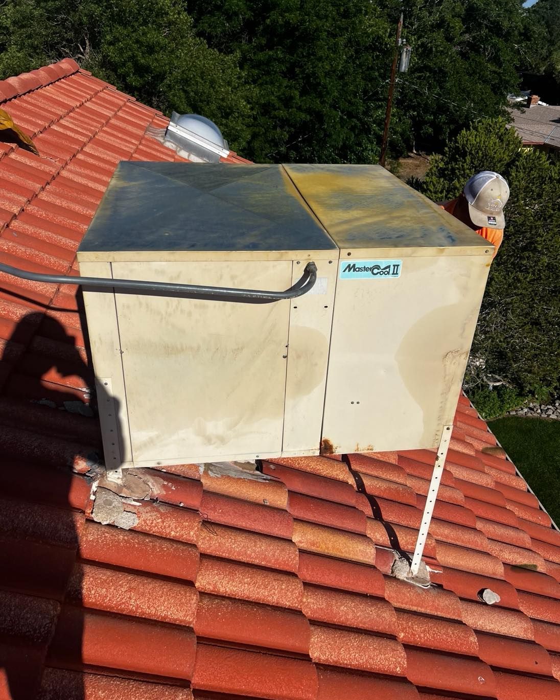 Square ventilation unit on red tiled roof. A person with a white hat is next to it.