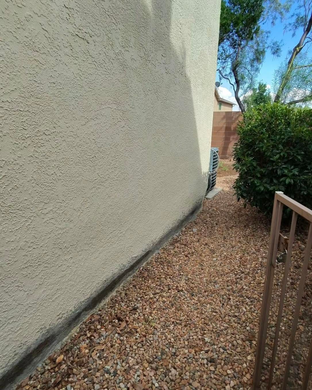 Tan stucco wall next to a gravel walkway, edged by a dark strip.