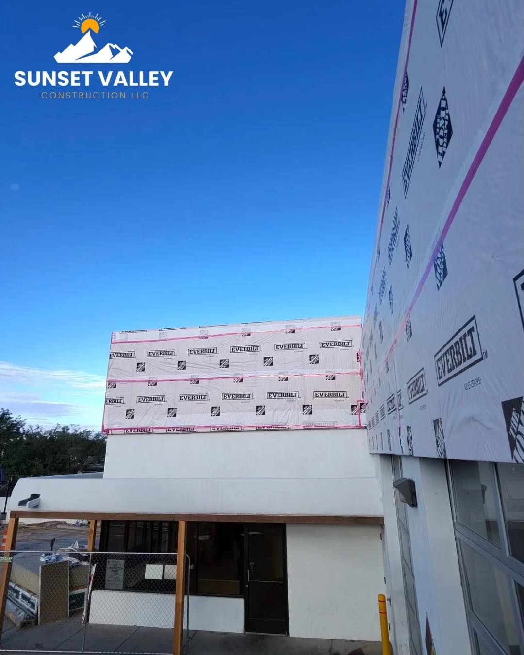 Construction site with white building, blue sky, and protective wrap.