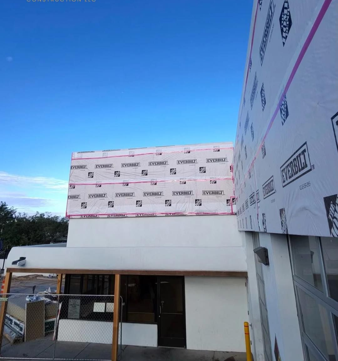 Building under construction; white walls, pink tape, blue sky, Sunset Valley Construction logo.