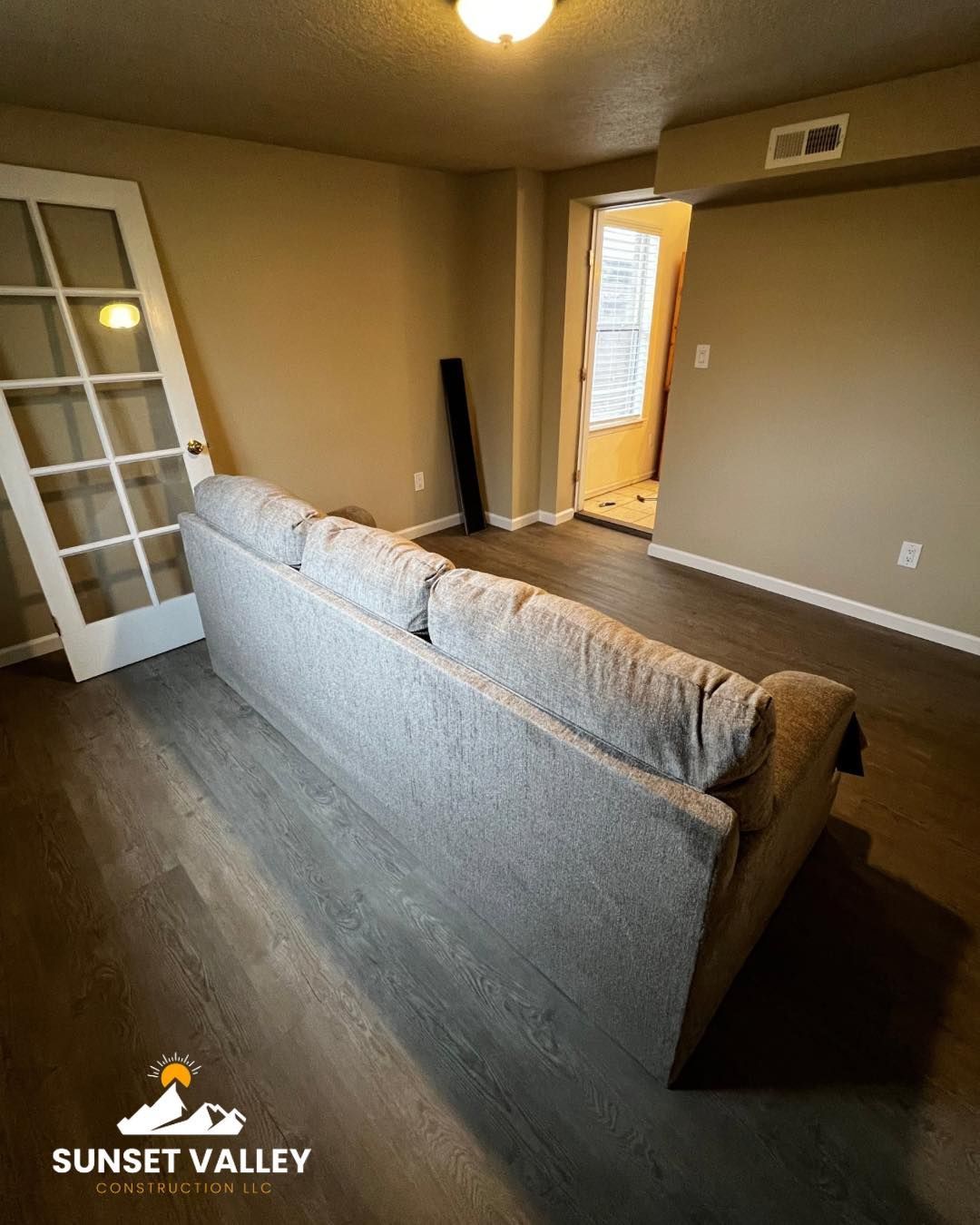 A gray couch in a room with hardwood floors and a white door, light brown walls.