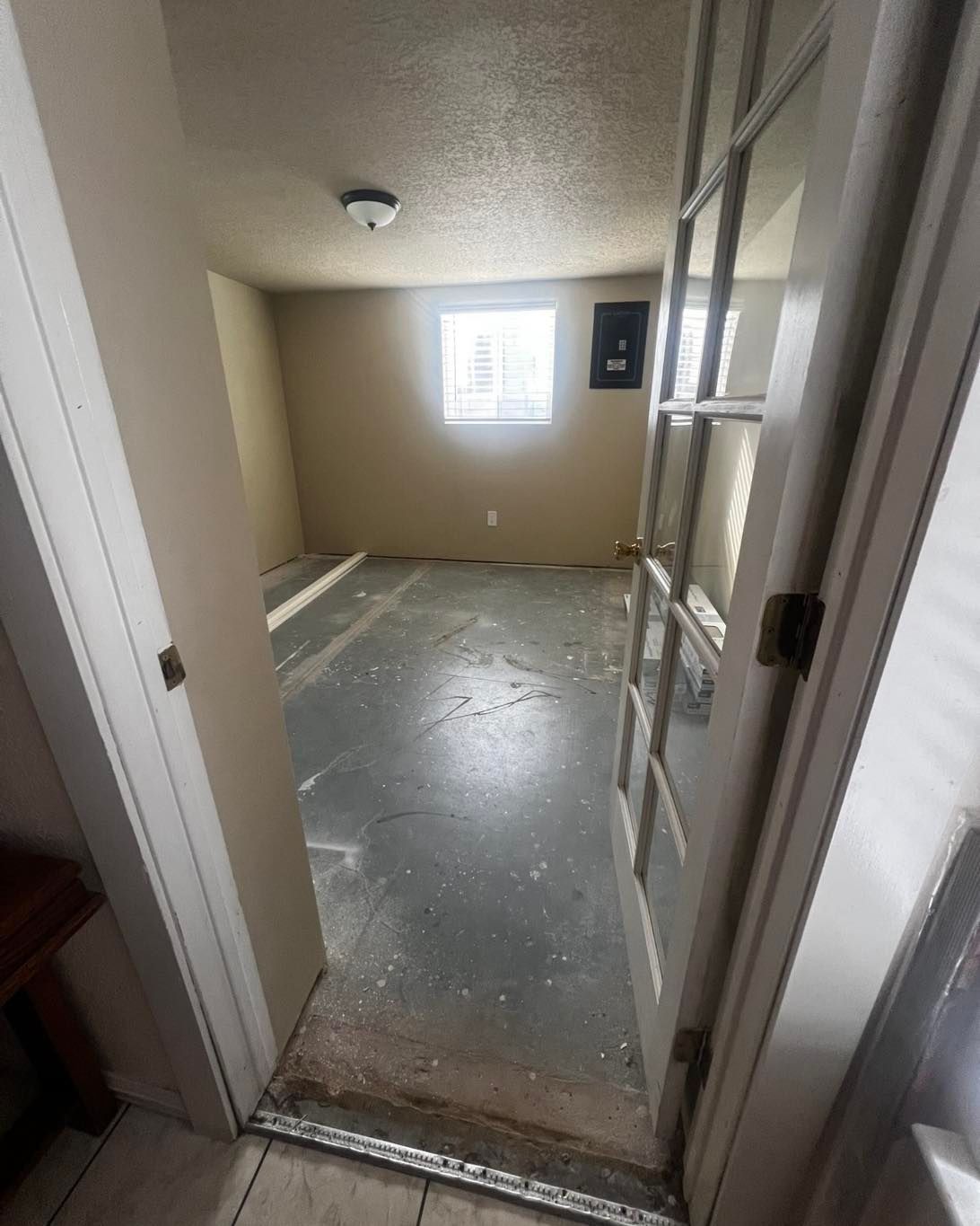 Room with debris on the floor, open doorway, window, and electrical panel on the wall.