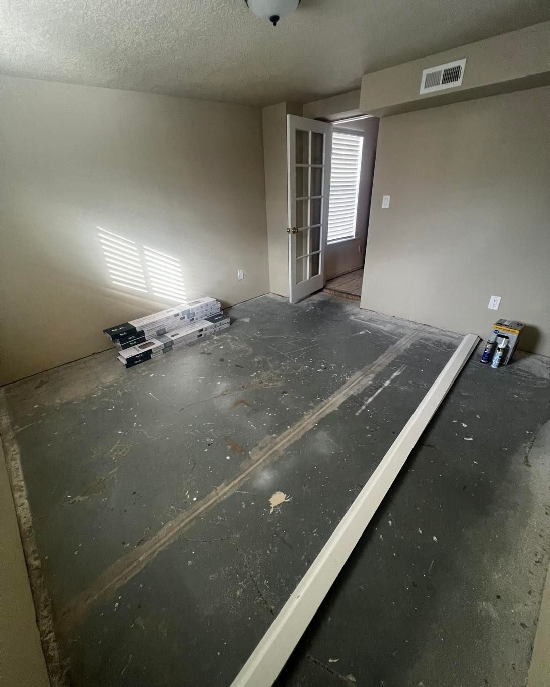 Room with dark floor, beige walls, open French doors, and materials for renovation.