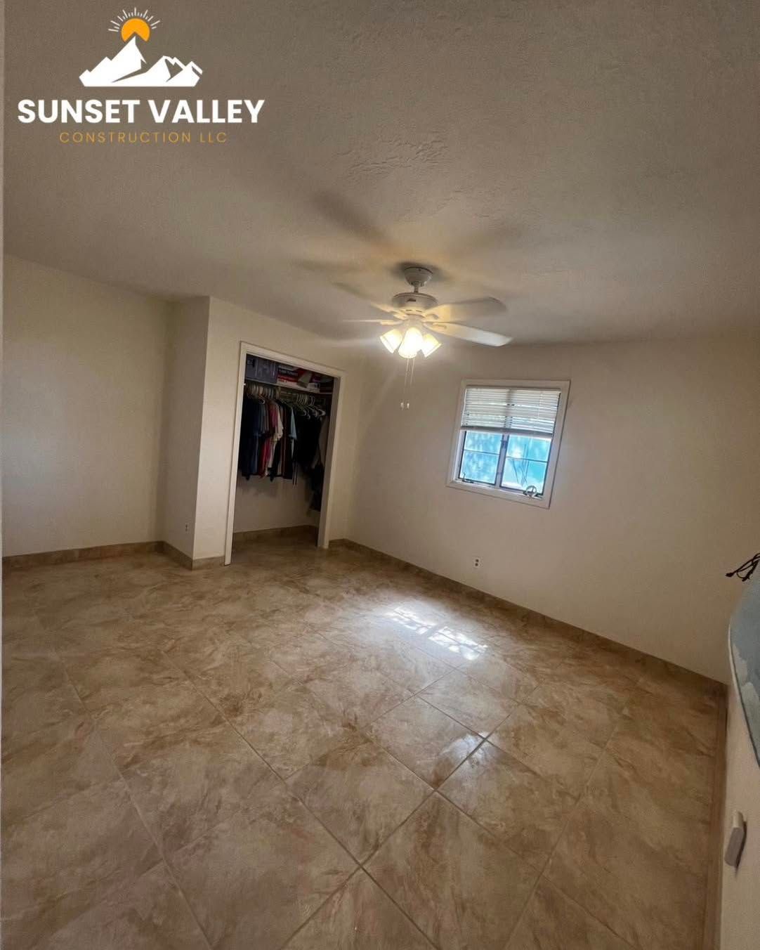 Empty bedroom with tiled floor, walk-in closet, ceiling fan, and window.