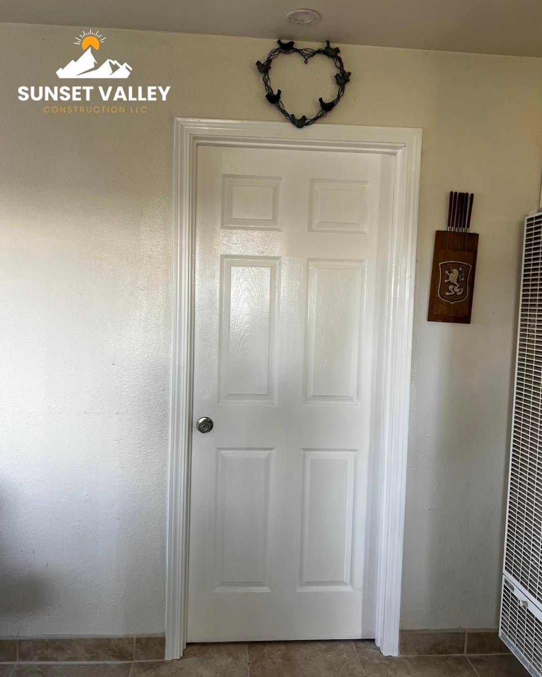 White six-panel door with a heart-shaped wreath above it and brown tile floor.