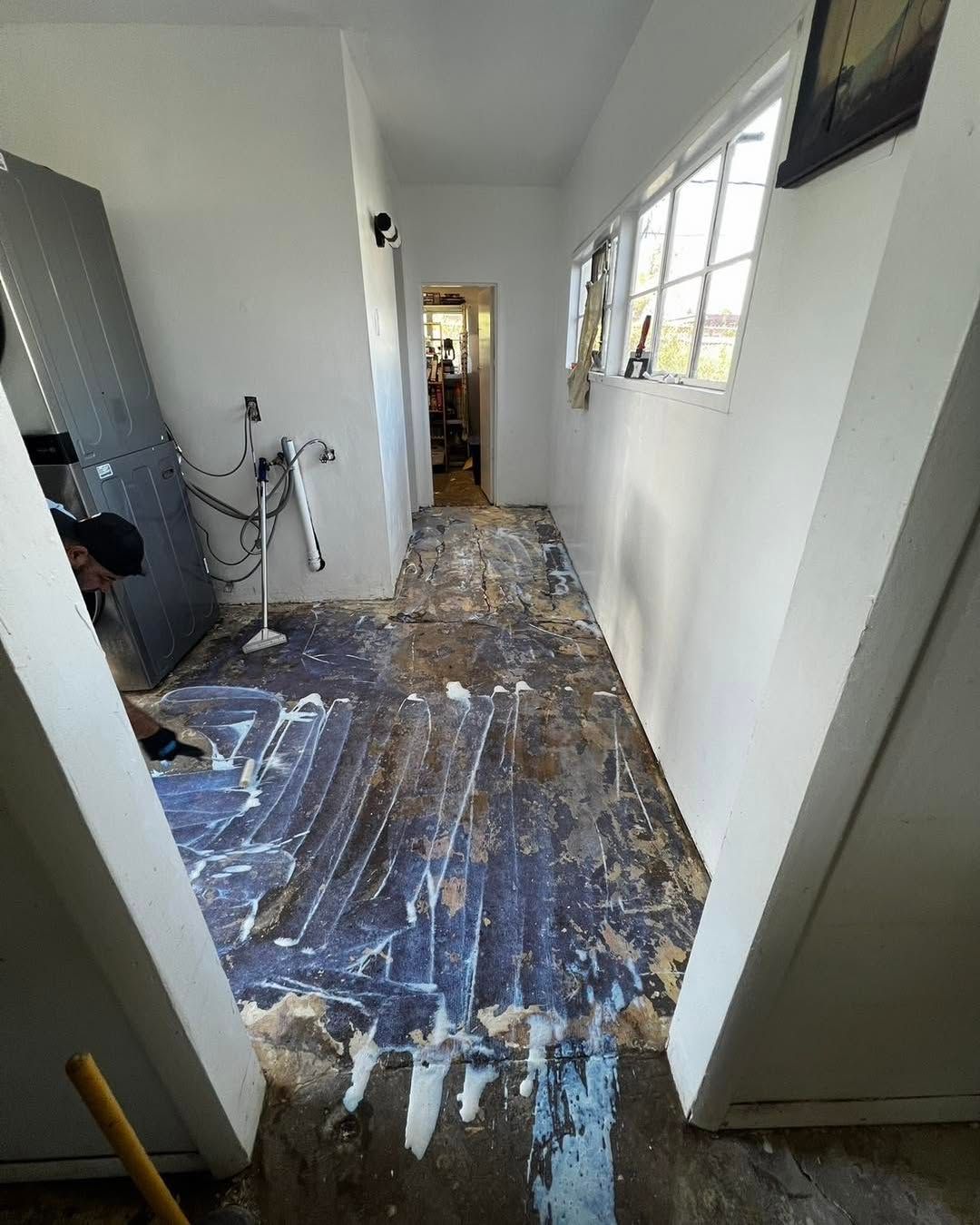 Hallway with ripped-up flooring, walls and door frame are white, a large grey panel leans against a wall.