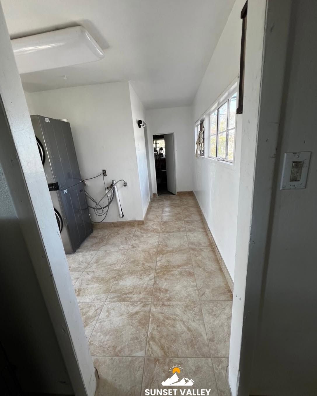Narrow, tiled hallway with a refrigerator, windows, and a doorway.