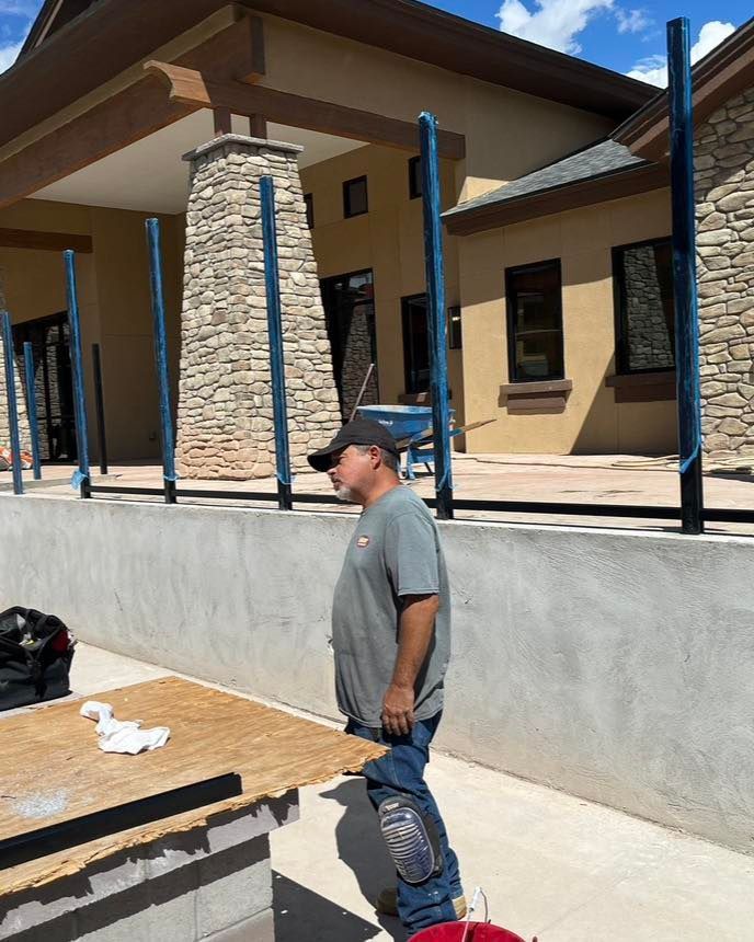 Man in a gray shirt, knee pads, and hat standing near a building with blue poles.