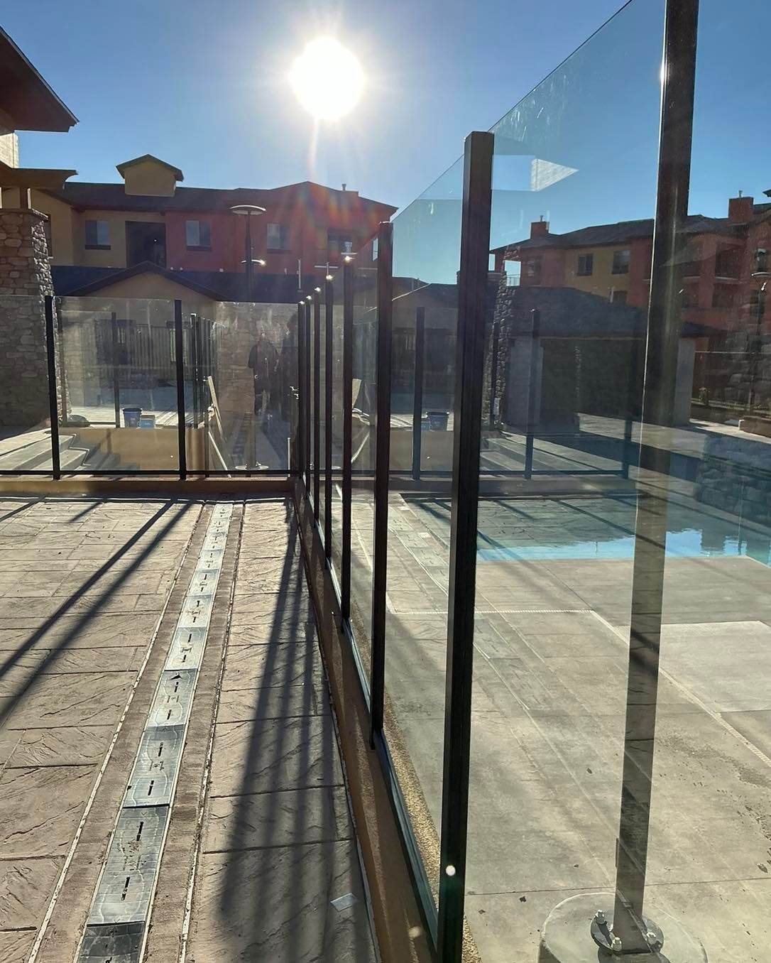 Glass pool fence with sunlight; exterior view with buildings in the background.
