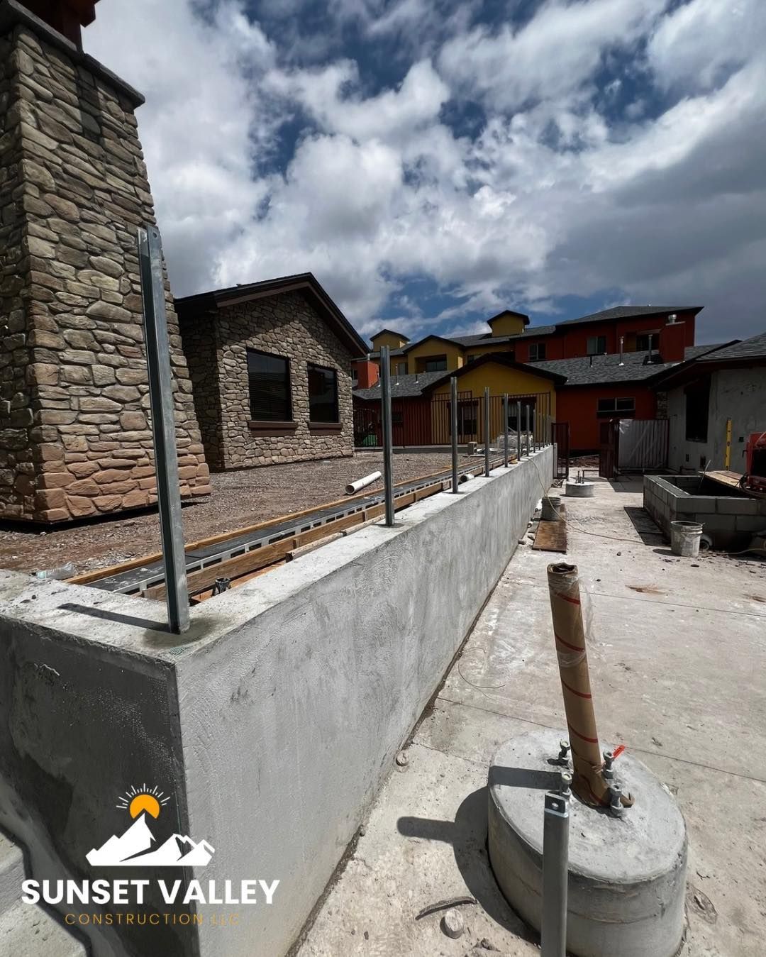 Concrete wall with metal posts, houses in background, cloudy sky.
