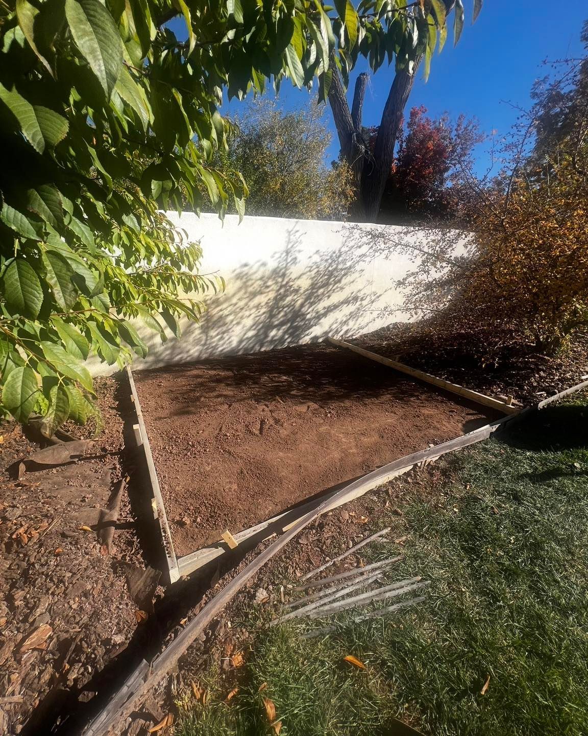 Brown garden bed bordered by wood on a lawn, next to a wall, and plants.