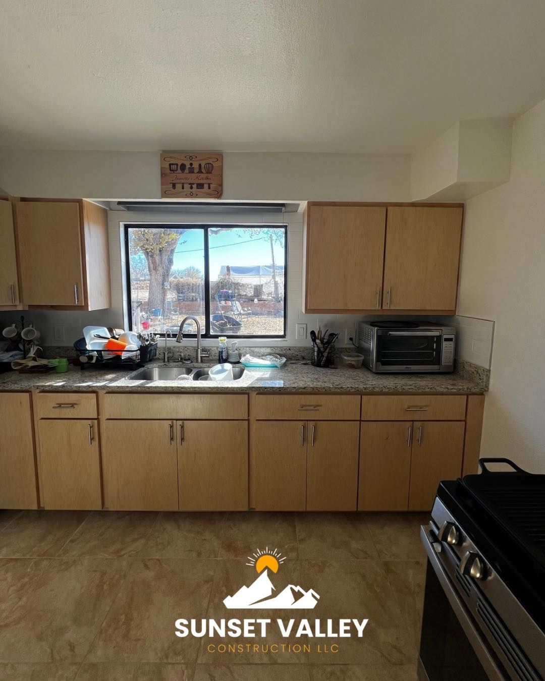 Kitchen with tan cabinets, a window over the sink, and a stovetop.