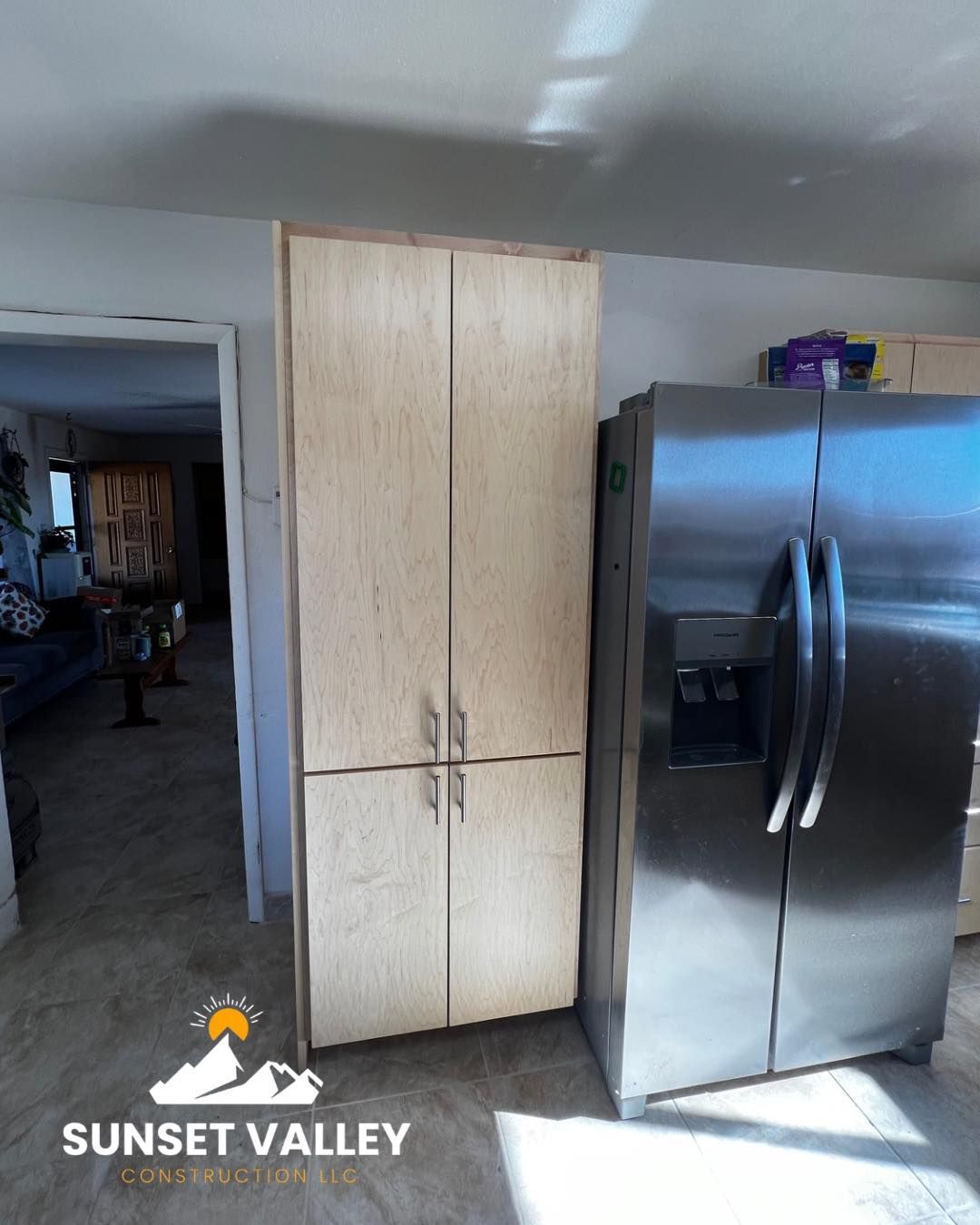Tall light-colored cabinet next to a stainless steel refrigerator in a kitchen.