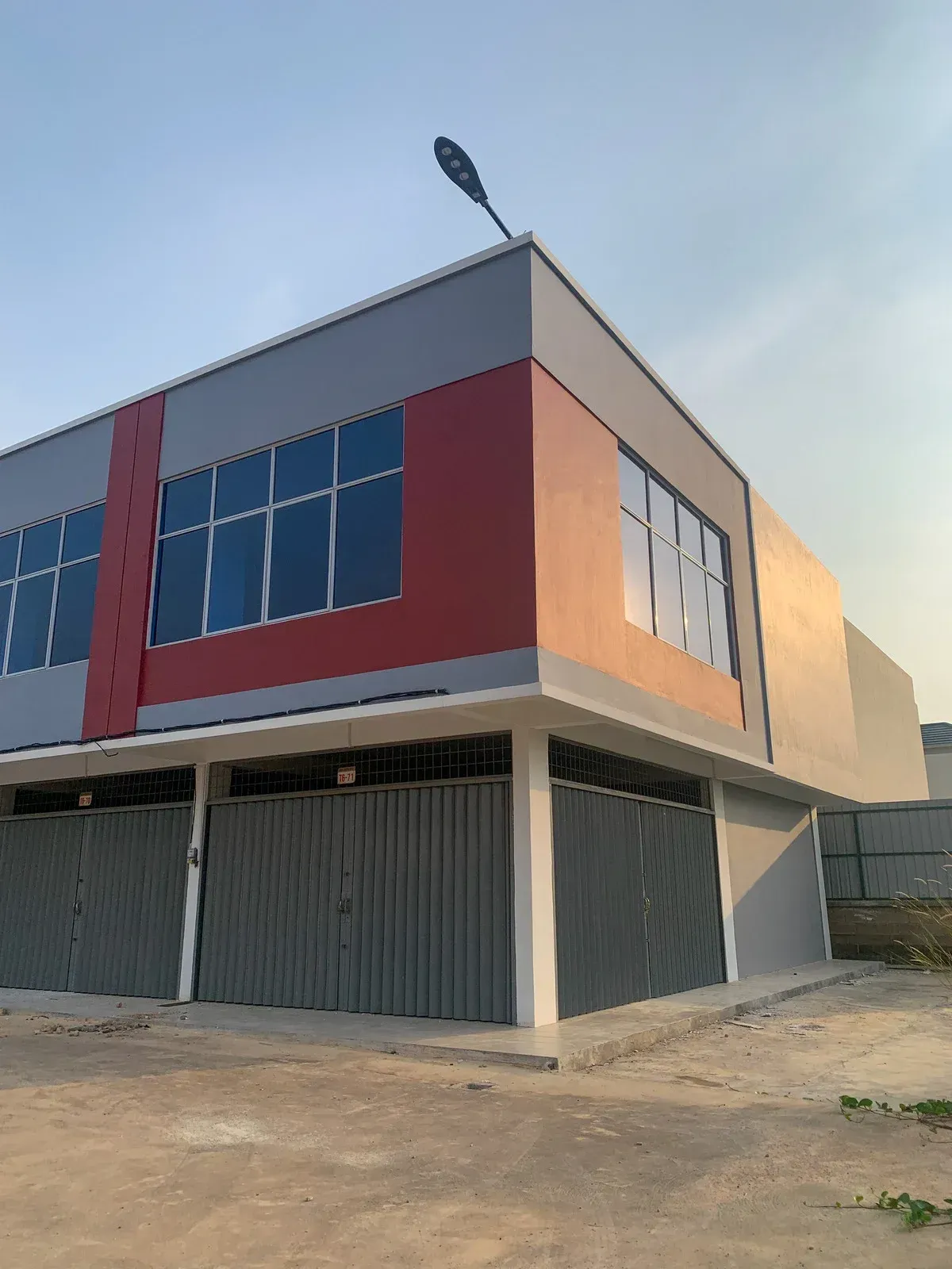 Two-story commercial building with gray and red facade, gray metal garage doors, and large windows.