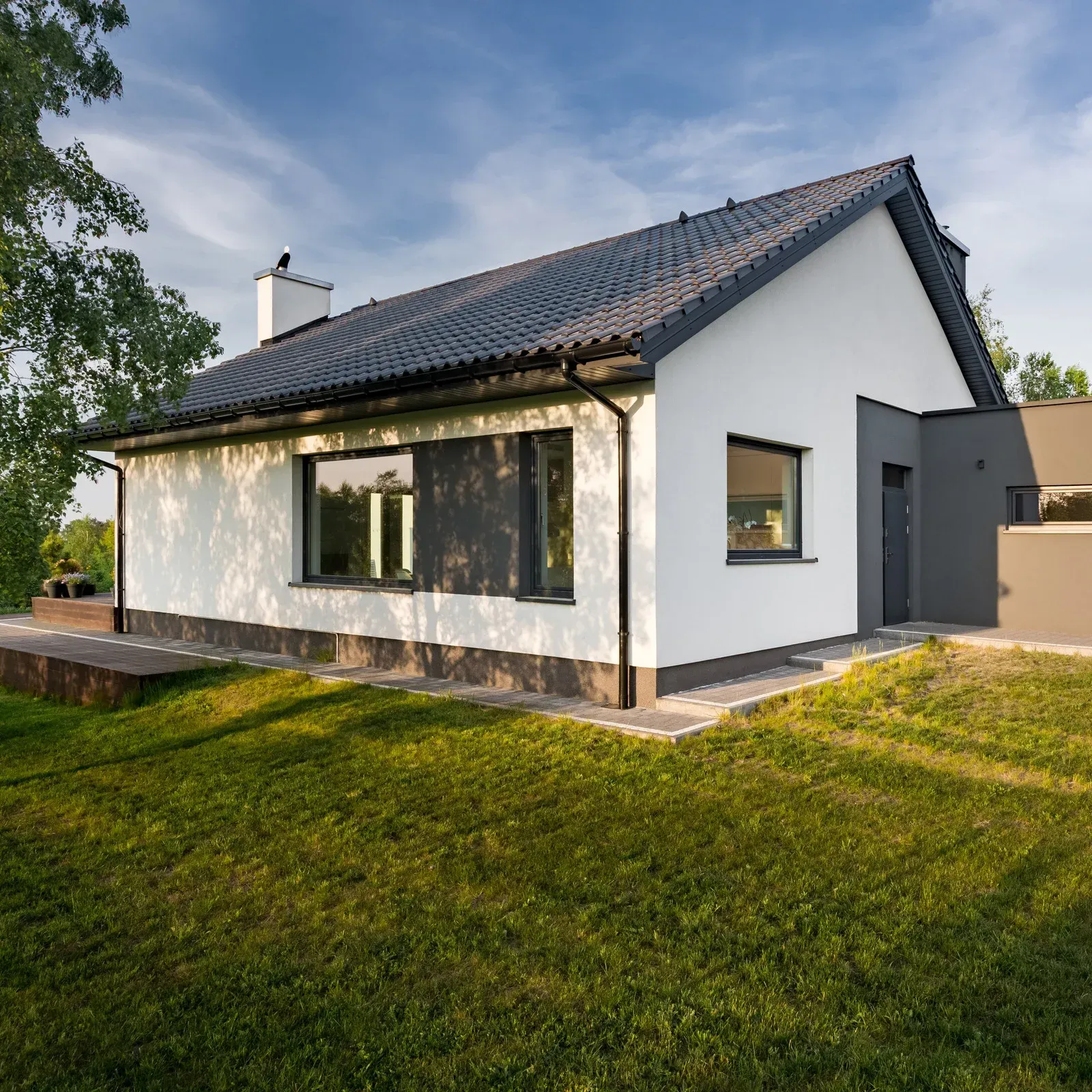 Modern white house with dark roof, windows, and trim; green lawn.