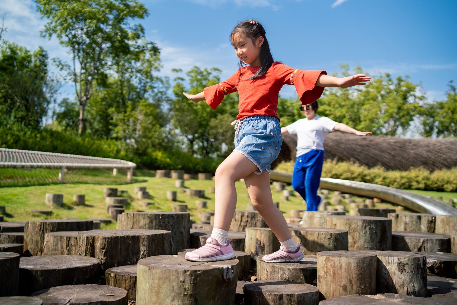 A girl and a boy are playing on a wooden playground made of tree stumps.