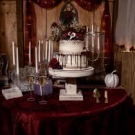 Elegant white tiered cake with flowers on a burgundy table, surrounded by candles and small decor in a room.