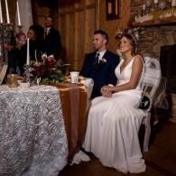 Bride and groom seated at a decorated wedding reception table, looking toward the ceremony area