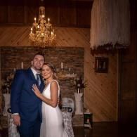 Couple posing in a warmly lit rustic venue, with a chandelier and stone fireplace behind them.