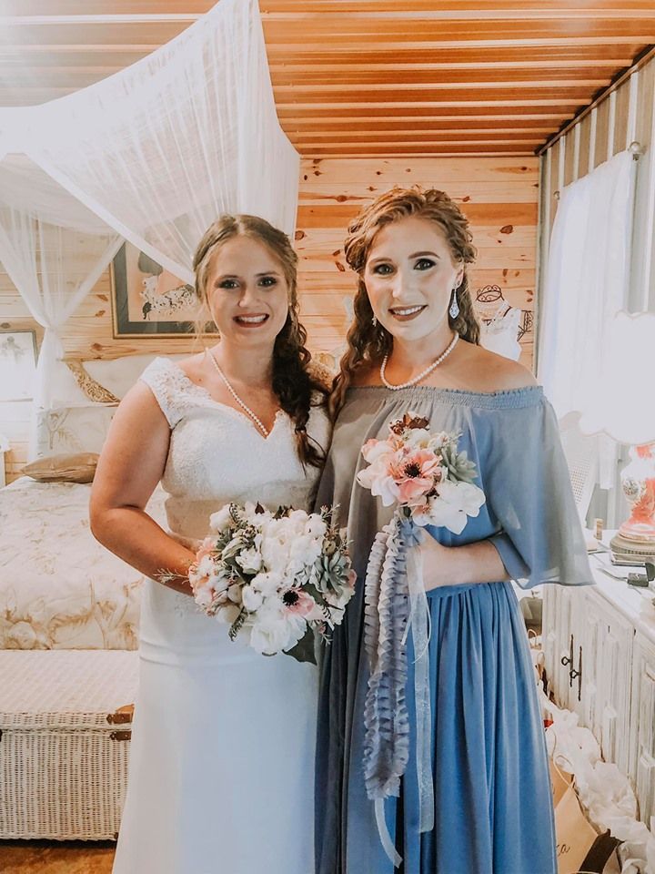 Two women in formal dresses holding bouquets, standing together in a decorated indoor venue