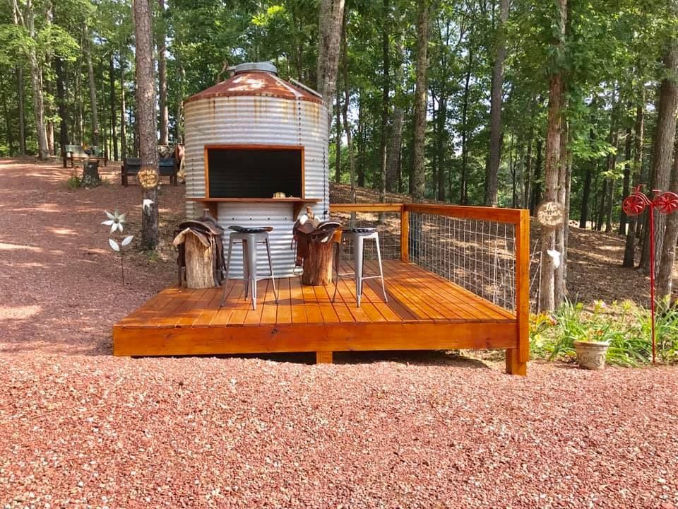 Wooden backyard deck with a barbecue smoker, metal chair, and forest trees in the background