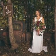 Bride in a white dress holding a bouquet in a rustic outdoor setting, standing by an old door and lantern.
