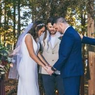 Wedding couple and officiant holding hands during an outdoor ceremony in the woods
