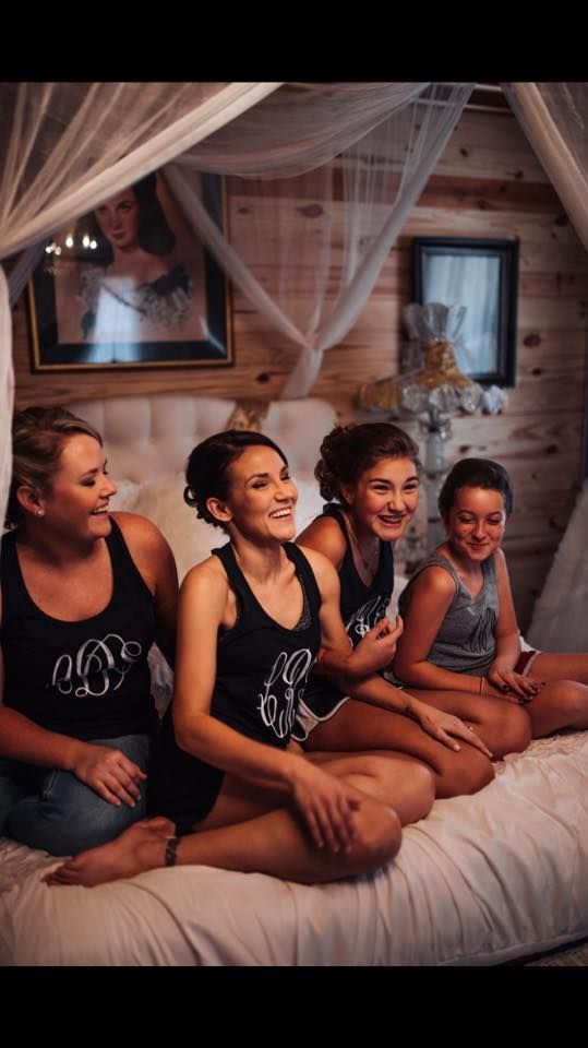 Four women sitting on a bed in a cozy wooden room, smiling and chatting under draped fabric.