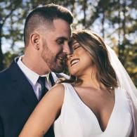 Bride and groom smiling in a close embrace outdoors, with the bride in a white dress and veil.