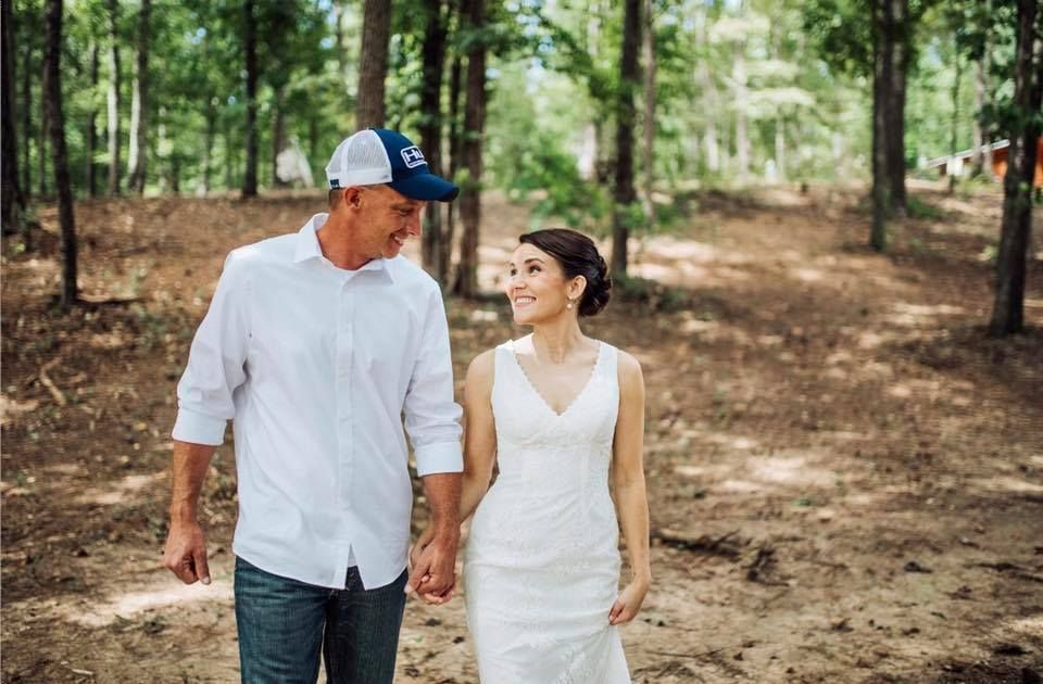 Two people walking hand in hand through a wooded area, both dressed in white.