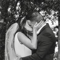 Bride and groom kissing under trees in black and white