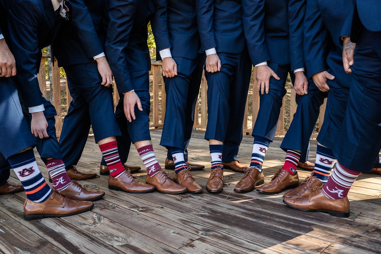 People in navy suits and colorful socks standing in a row on patterned carpet, showing brown dress shoes.