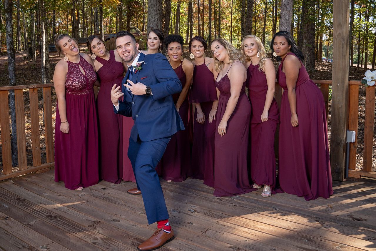 Wedding party posing on a wooden deck, with the groom in a blue suit and attendants in burgundy dresses.