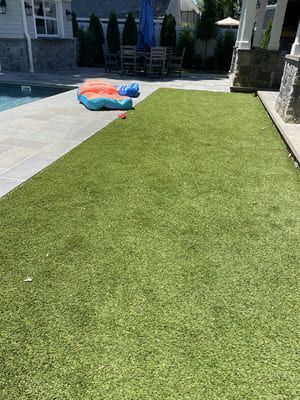 Artificial green turf next to a pool and patio. An inflatable toy and chair set are visible.