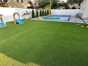 Backyard with a pool, playhouse, and artificial grass. A blue slide is on the lawn.