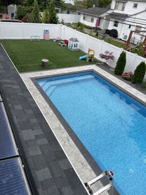 Backyard with a rectangular swimming pool, artificial turf, white fence, and small children's play area.