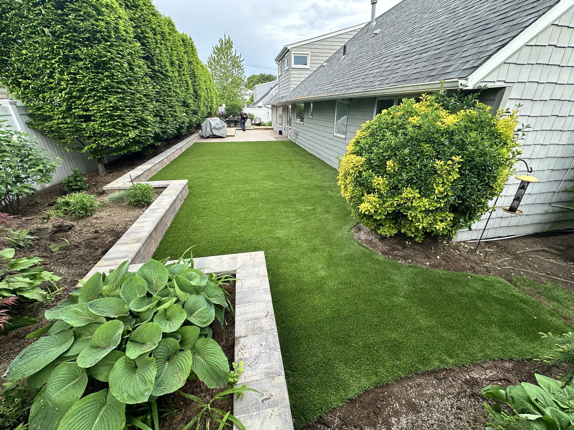 Lush green lawn with brick borders and a house with gray siding.