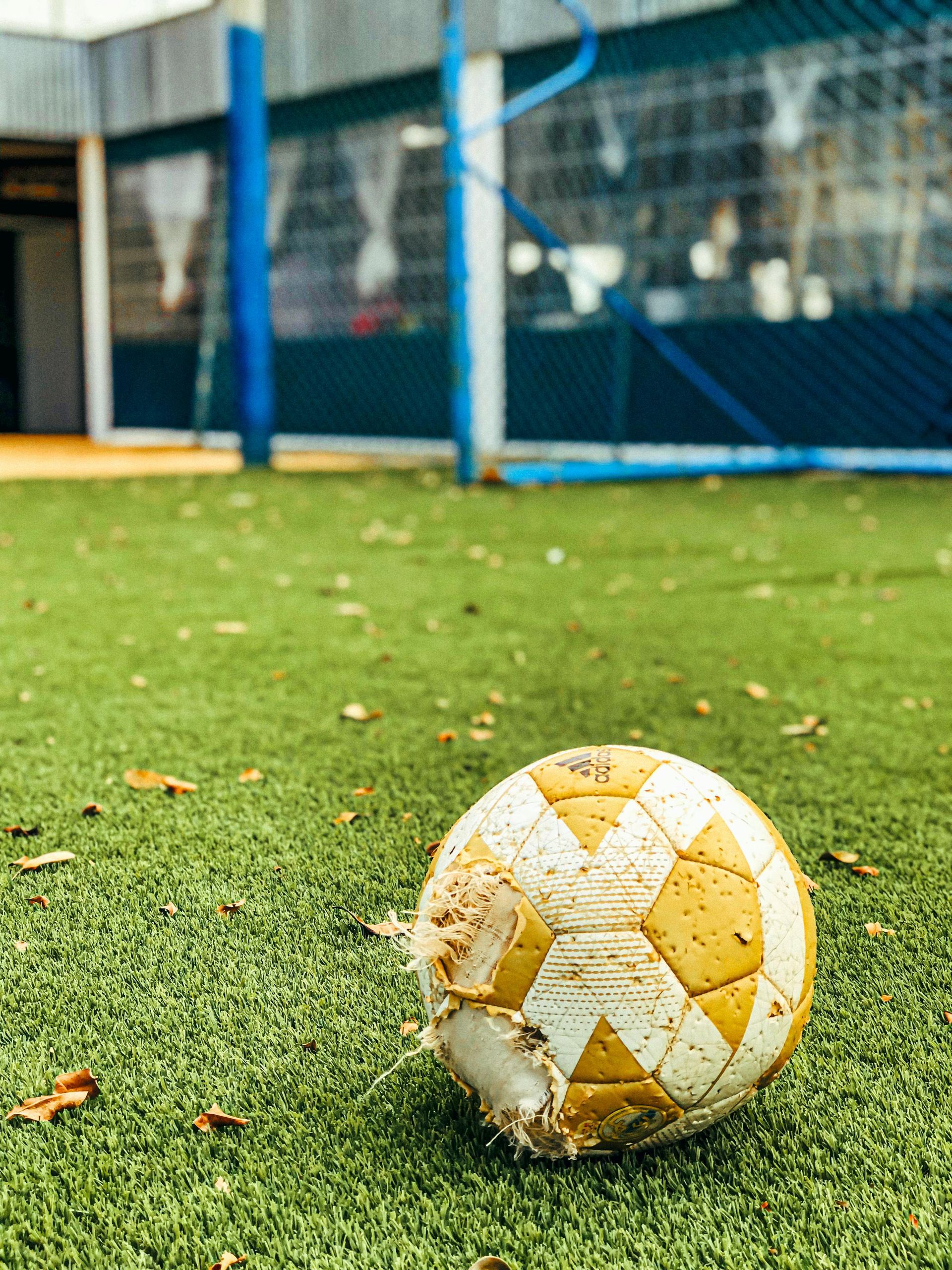 Worn soccer ball on green turf field with a blue goal in the background.