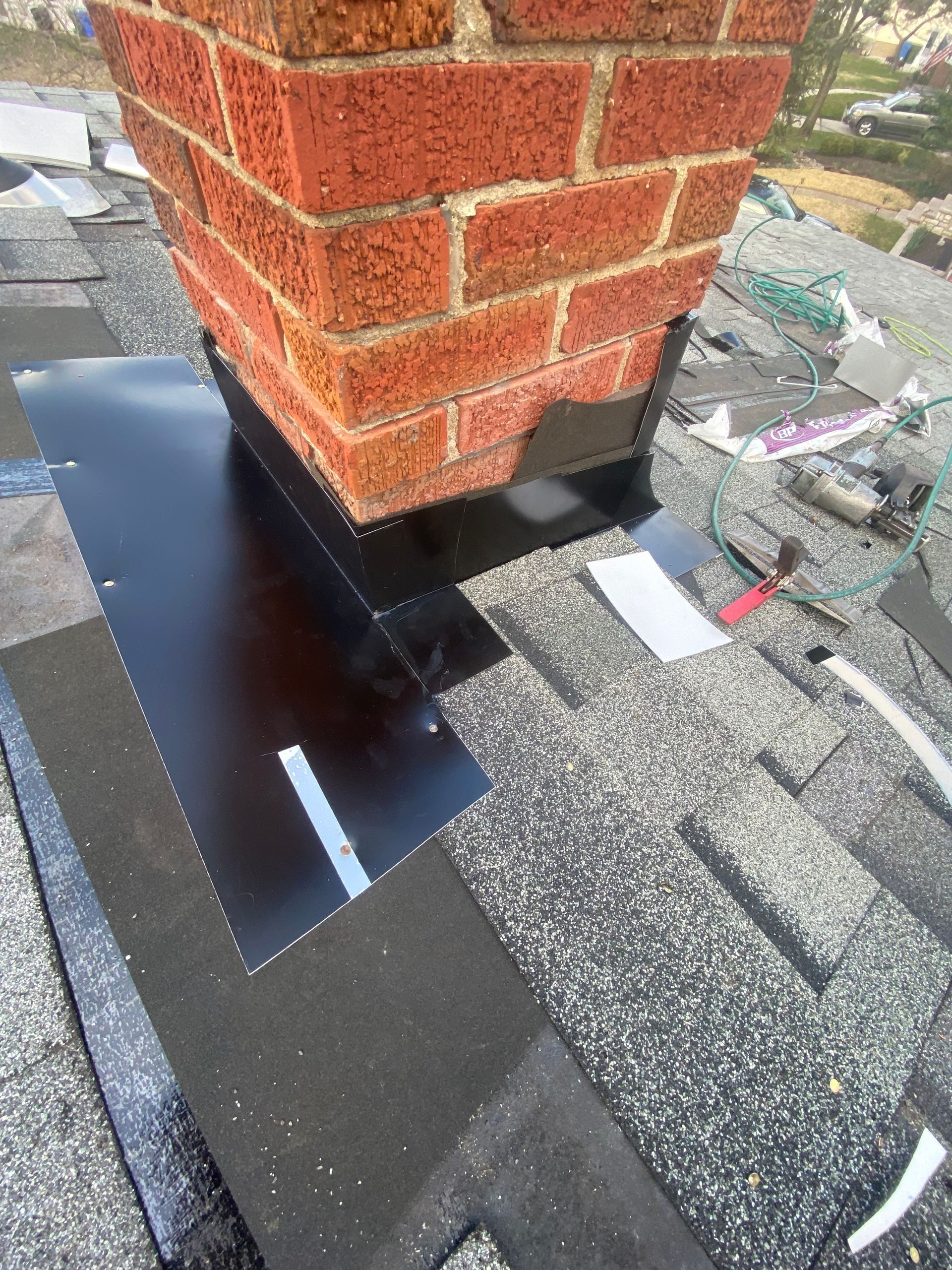 Roof vent pipe base flashing on a shingled roof beside a brick chimney
