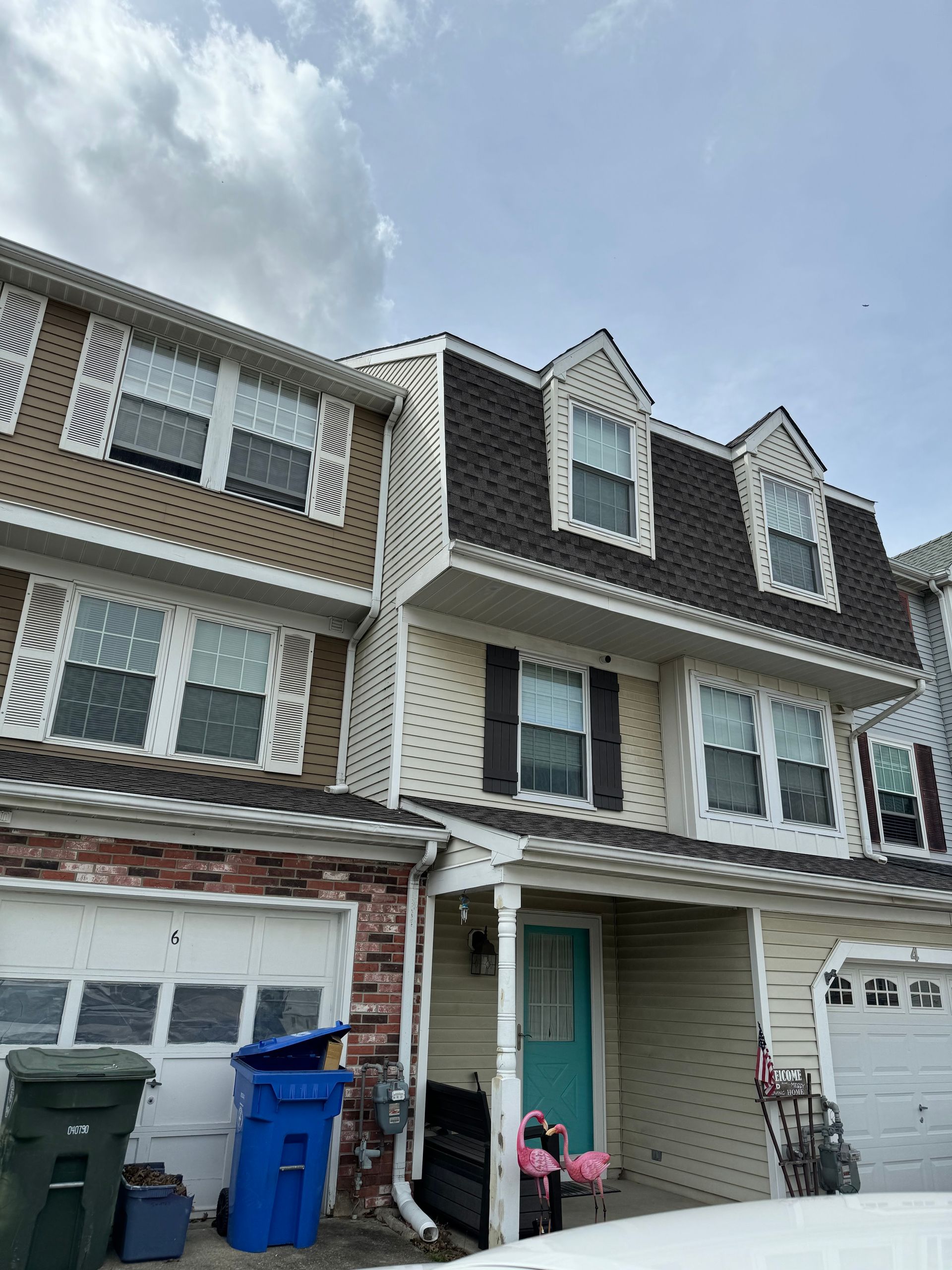 Row of townhouses with garages and blue recycling bins under a cloudy sky