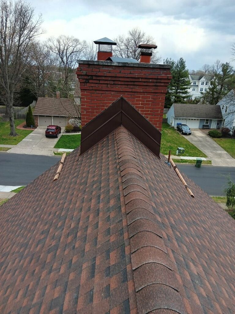 View from a shingled roof toward a brick chimney in a suburban neighborhood